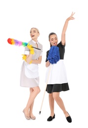 Young chambermaids with dusting brush and mop on white background