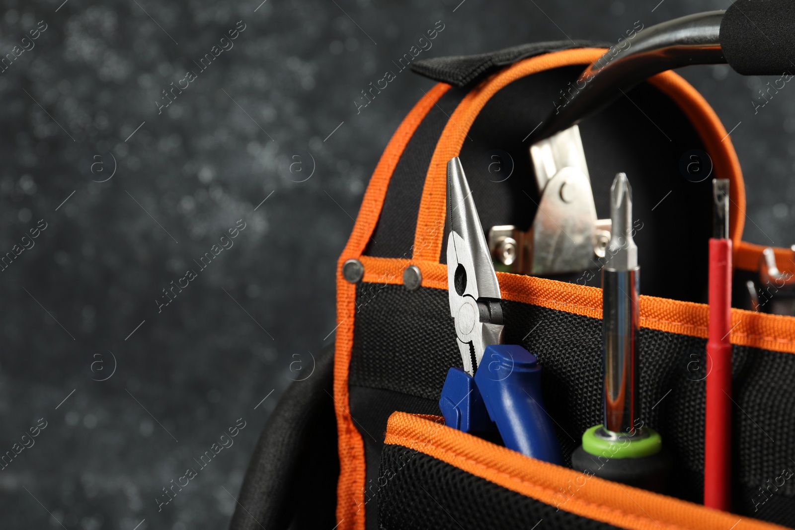 Photo of Bag with needle nose pliers, screwdrivers and other repair tools on dark background, closeup. Space for text