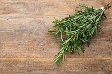 Photo of Bunch of fresh rosemary on wooden table, above view. Space for text