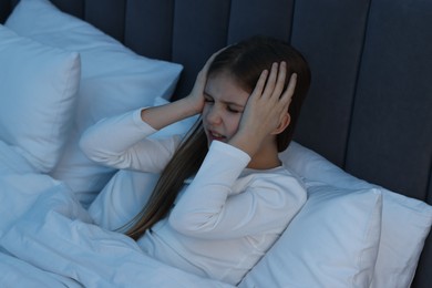 Little girl suffering from headache in bed at night