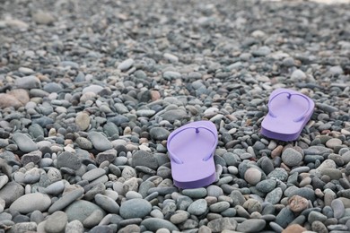 Stylish violet flip flops on pebble seashore. Space for text