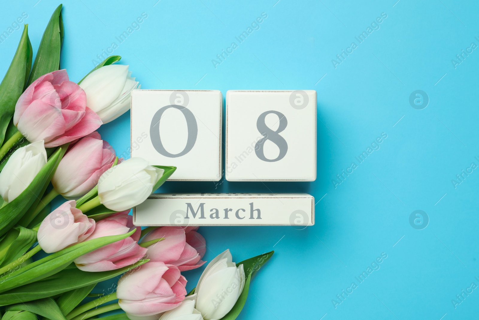 Photo of Wooden block calendar with date 8th of March and tulips on light blue background, flat lay. Space for text
