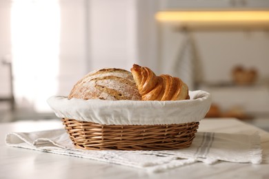 Wicker bread basket with freshly baked loaf and croissant on white marble table in kitchen