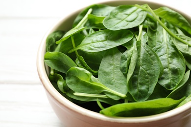 Photo of Bowl of fresh green healthy spinach on white wooden table, closeup