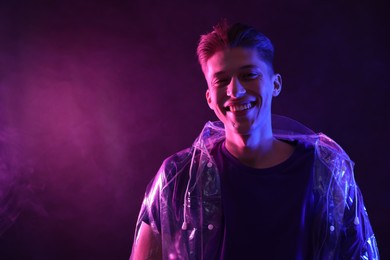 Young man wearing clear coat in neon lights with smoke effect. Space for text