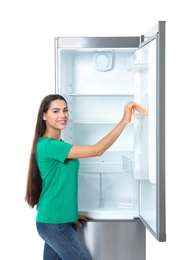 Photo of Young woman cleaning refrigerator with rag on white background