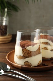 Delicious tiramisu in glasses and spoons on wooden table, closeup