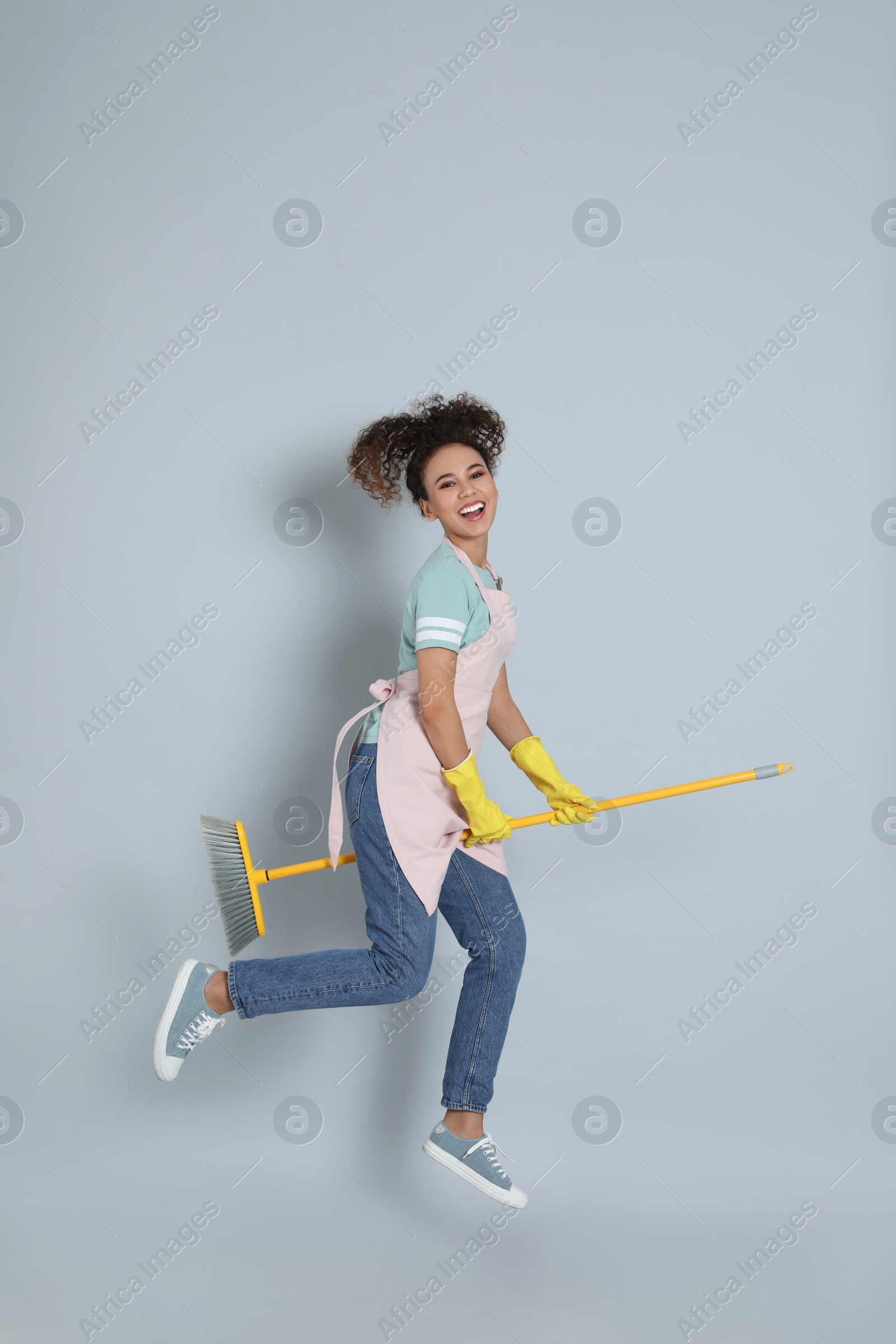 Photo of African American woman with yellow broom jumping on grey background