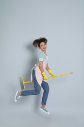 African American woman with yellow broom jumping on grey background