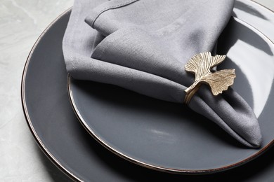 Plates with gray fabric napkin and decorative ring in table, closeup