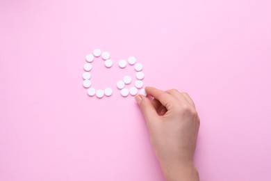 Woman making calcium symbol with white pills on pink background, top view