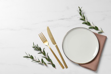 Stylish setting with cutlery and eucalyptus leaves on white marble table, flat lay. Space for text