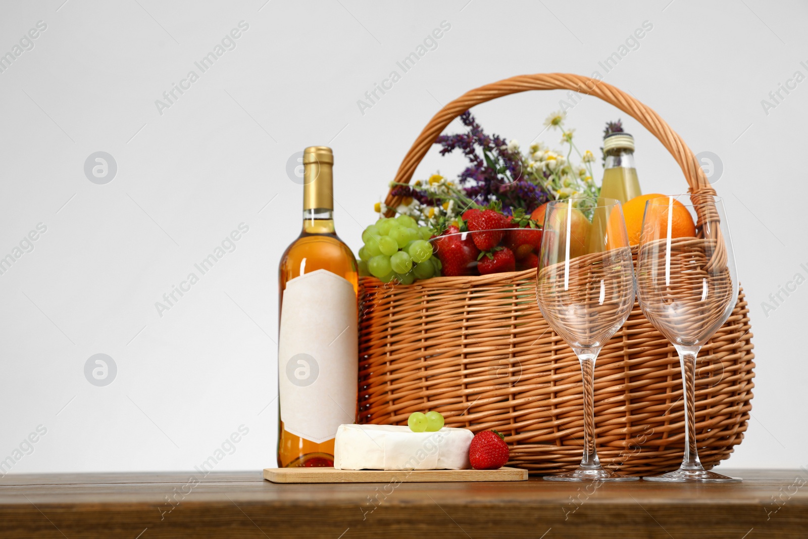 Photo of Picnic basket with wine and products on wooden table against white background. Space for text