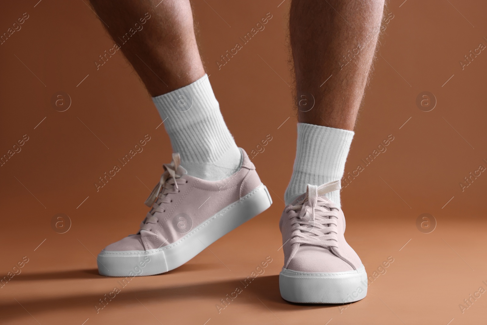 Photo of Man wearing stylish sneakers on brown background, closeup