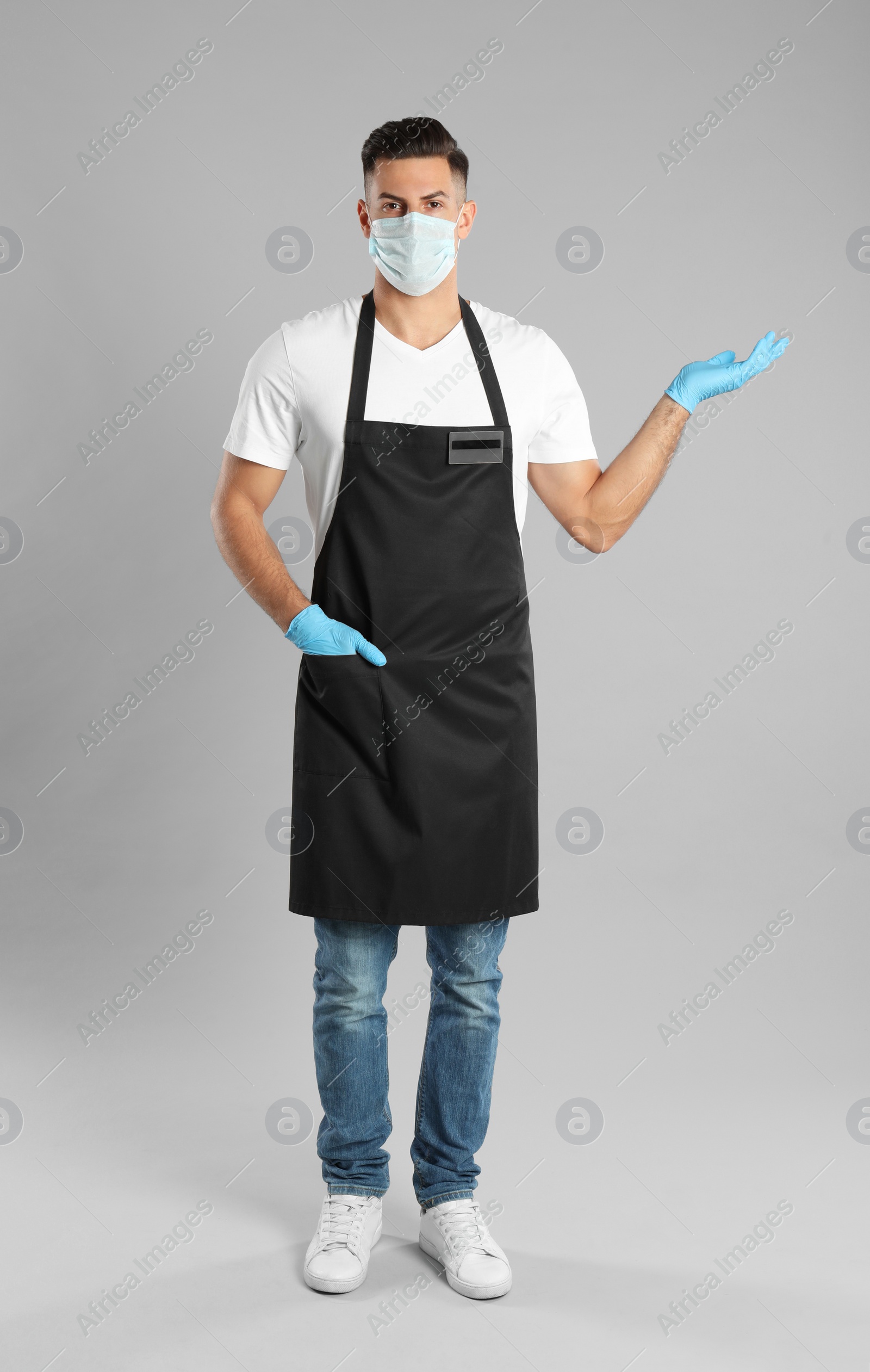 Photo of Waiter wearing medical face mask on light grey background