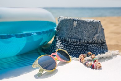 Photo of Denim hat and beach accessories on sand near sea, closeup