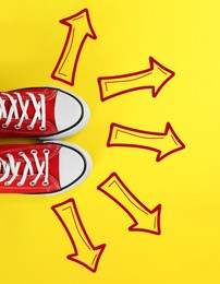 Image of Choosing future profession. Person standing in front of drawn signs on yellow background, top view. Arrows pointing in different directions symbolizing diversity of opportunities