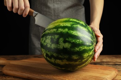 Woman cutting delicious watermelon at wooden table against black background, closeup