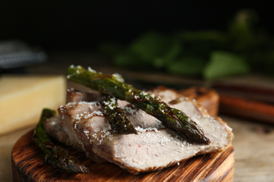 Photo of Tasty meat served with asparagus on wooden board, closeup