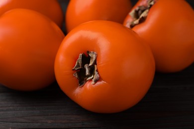 Photo of Delicious ripe persimmons on dark wooden table, closeup