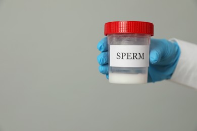 Scientist holding container with sperm on grey background, closeup. Space for text