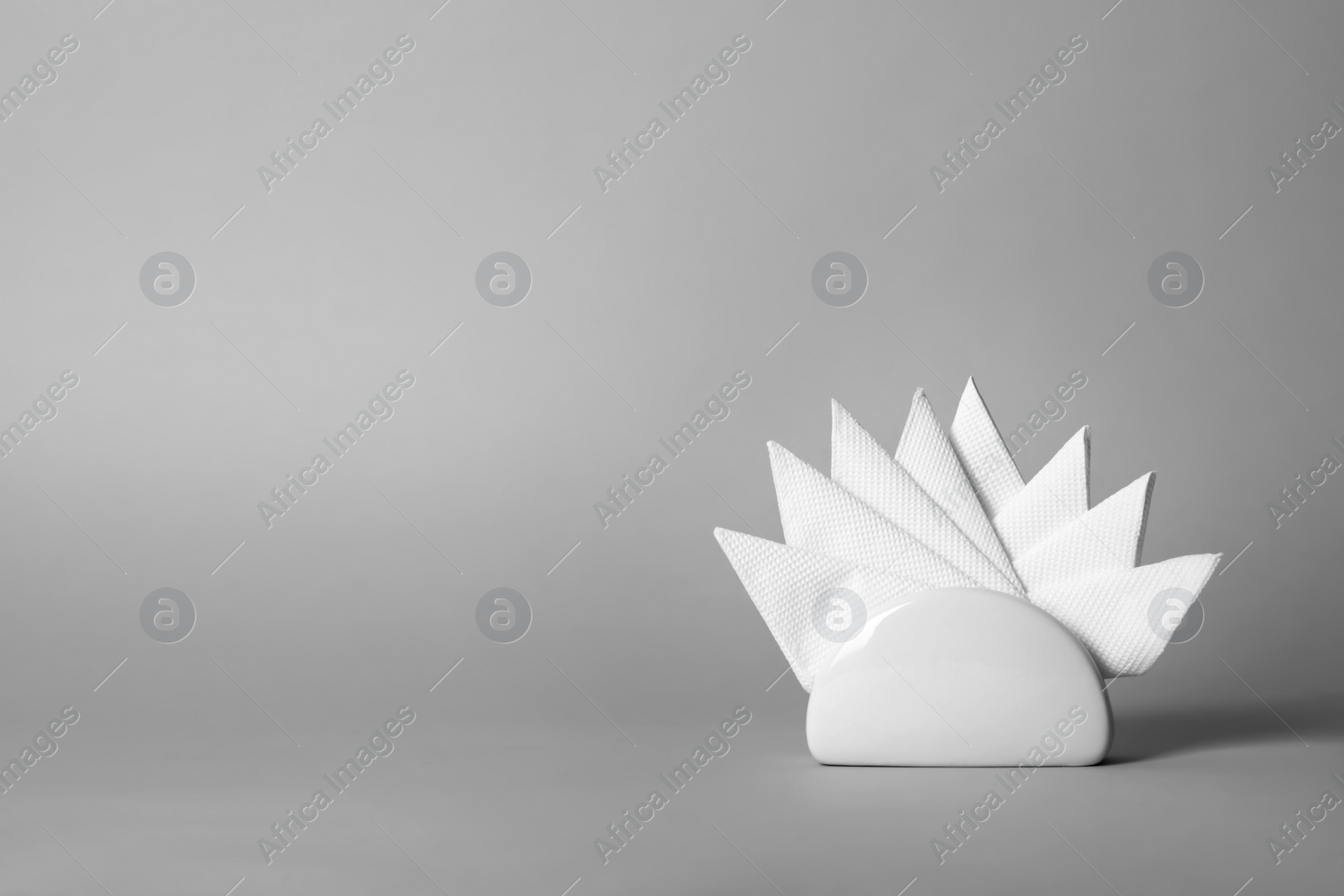 Photo of Napkin holder with paper serviettes on gray background. Space for text