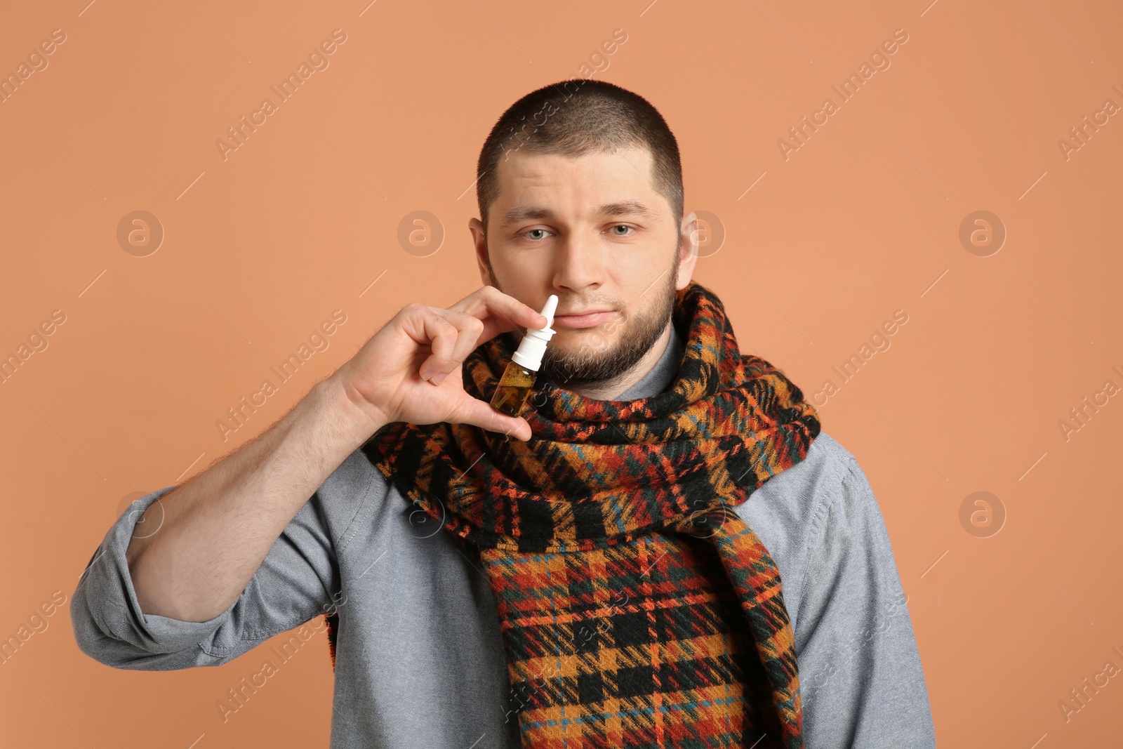 Photo of Sick man using nasal spray on orange background