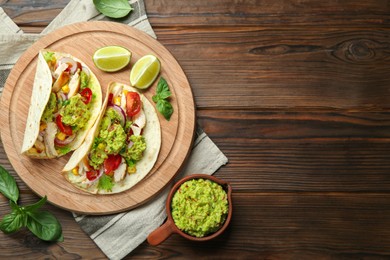 Delicious tacos with guacamole, meat and vegetables served with lime on wooden table, flat lay. Space for text
