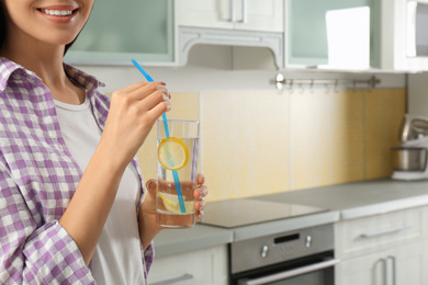 Photo of Young woman with lemon water in kitchen, closeup. Space for text