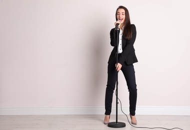 Photo of Young woman singing in microphone near color wall. Space for text