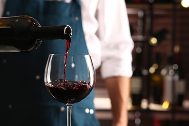 Bartender pouring red wine into glass indoors, closeup. Space for text