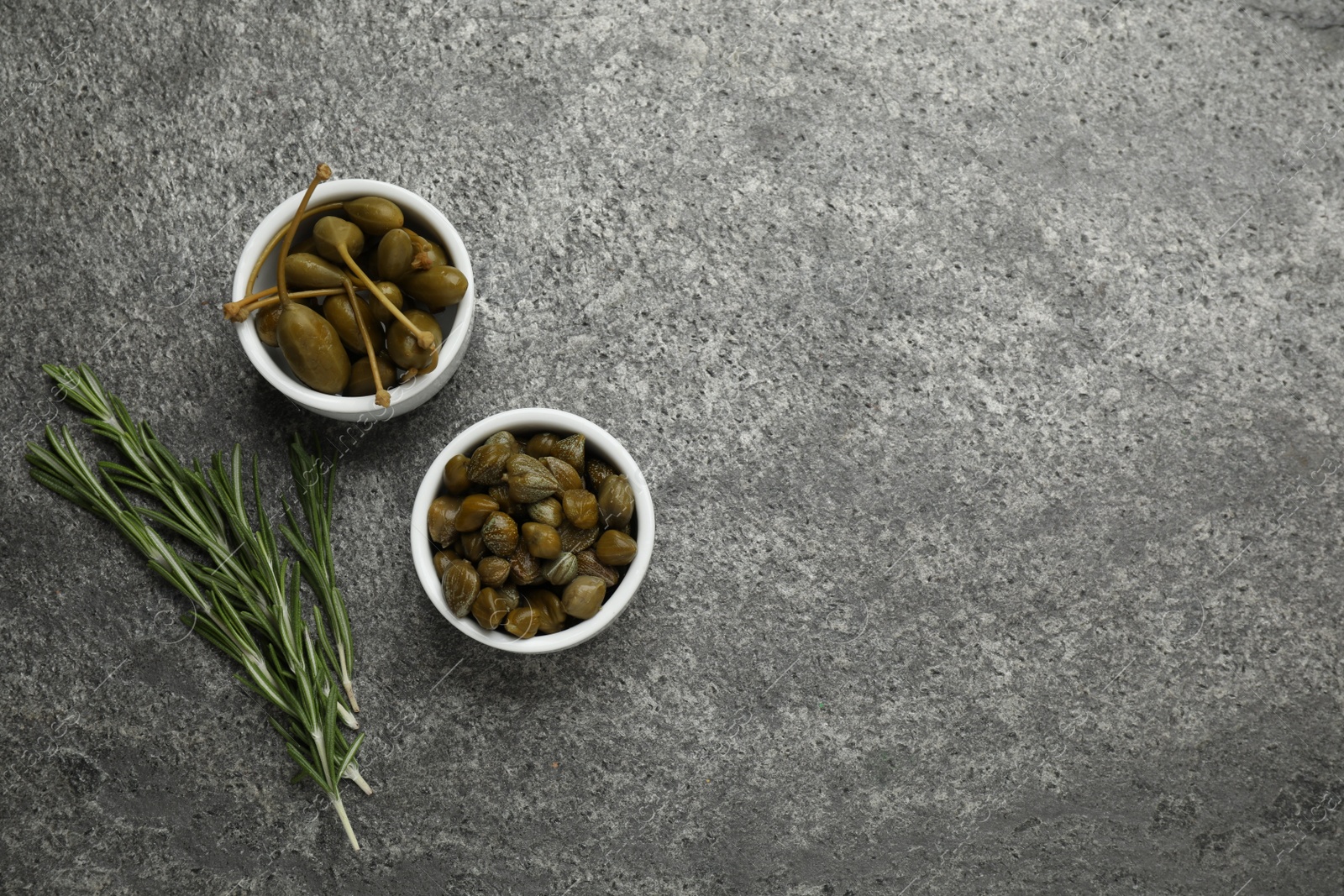 Photo of Tasty capers and rosemary on grey table, flat lay. Space for text