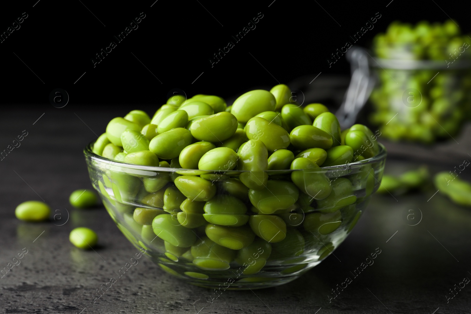 Photo of Bowl of delicious edamame beans on grey table against dark background, closeup