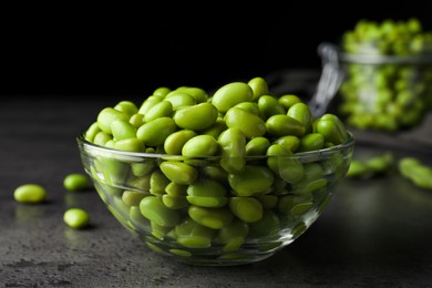 Bowl of delicious edamame beans on grey table against dark background, closeup