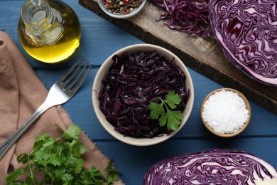 Photo of Tasty red cabbage sauerkraut with parsley and different ingredients on light blue wooden table, flat lay