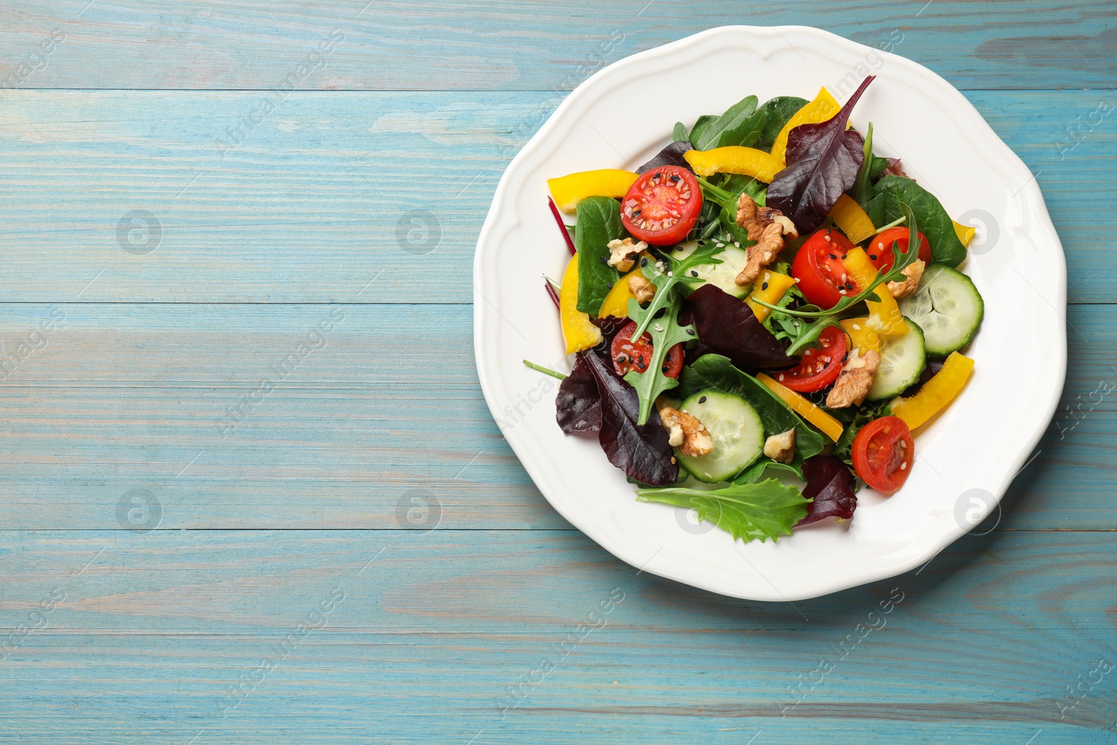 Photo of Tasty fresh vegetarian salad on light blue wooden table, top view. Space for text