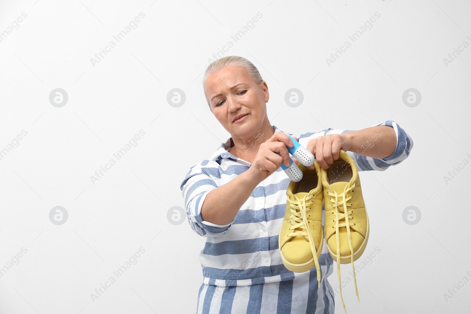 Photo of Woman putting capsule shoe freshener in footwear on white background