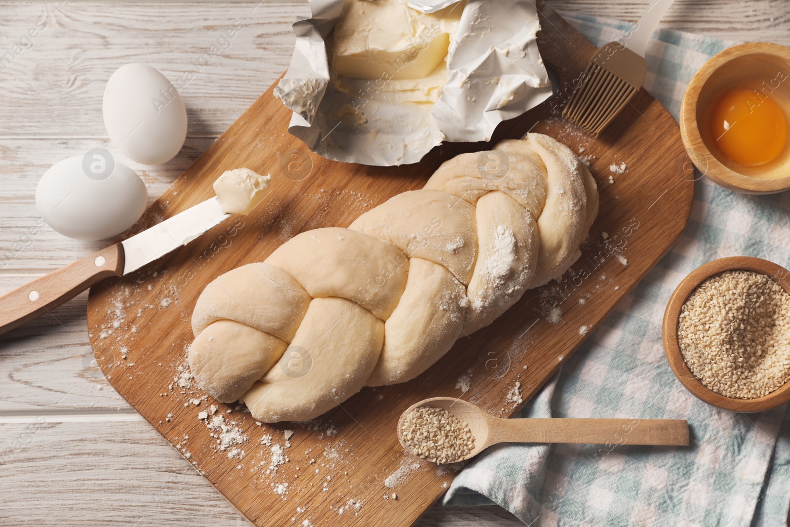 Photo of Raw braided bread and ingredients on white wooden table, flat lay. Traditional Shabbat challah