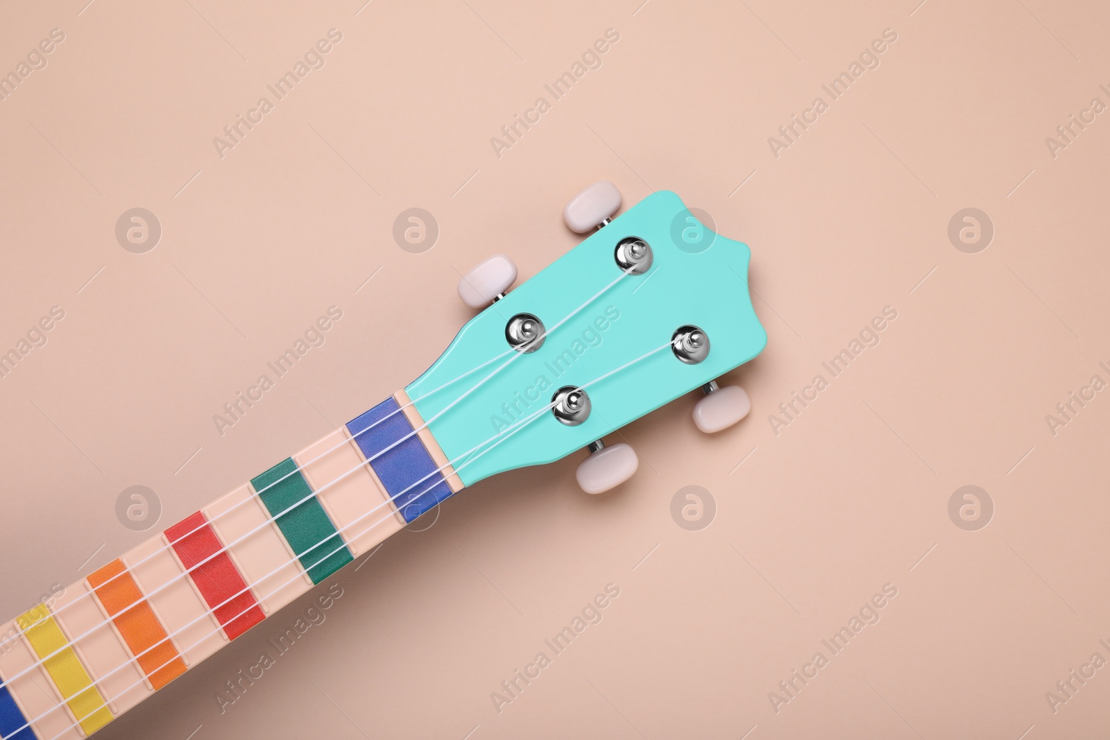 Photo of Colorful ukulele neck on beige background, top view. String musical instrument