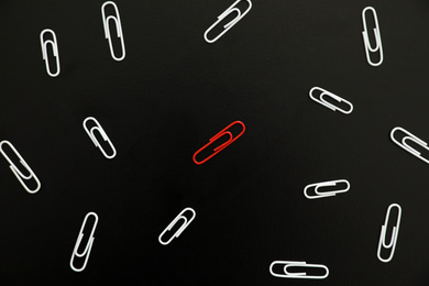 White paper clips and red one on black background, flat lay