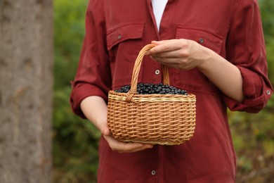 Photo of Woman holding wicker basket with delicious bilberries outdoors, closeup. Space for text