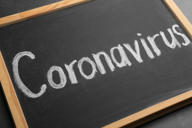 Chalkboard with word CORONAVIRUS on grey table, closeup