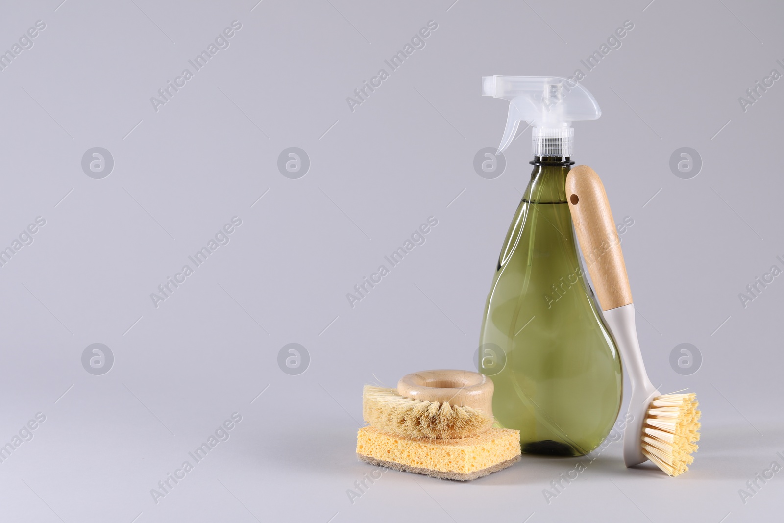 Photo of Bottle of cleaning product, sponge and brushes on light grey background. Space for text