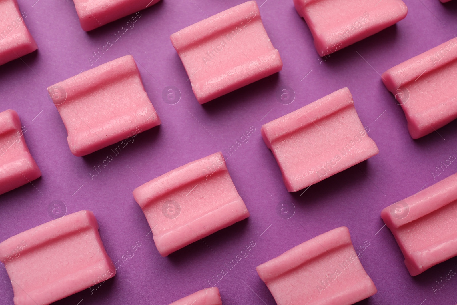 Photo of Tasty pink chewing gums on purple background, flat lay