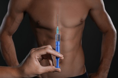 Woman holding syringe near athletic man on black background, closeup. Doping concept