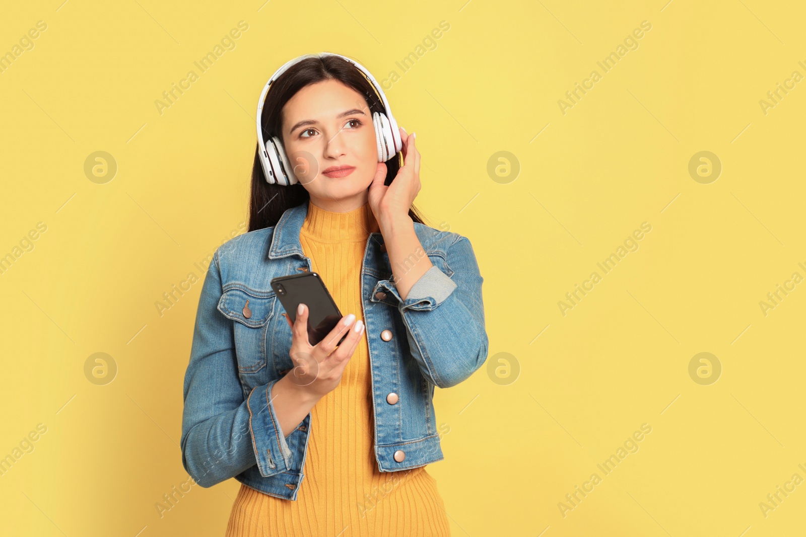 Photo of Young woman listening to audiobook on yellow background. Space for text