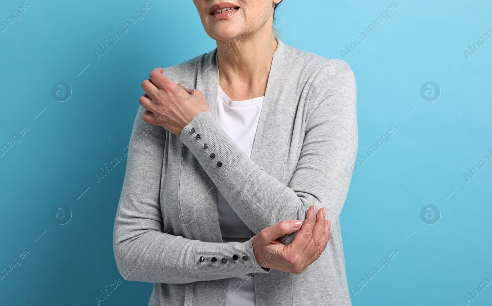 Photo of Arthritis symptoms. Woman suffering from pain in elbow on light blue background