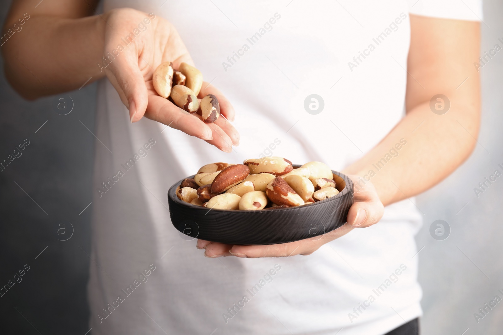 Photo of Woman with Brazil nuts on grey background, closeup