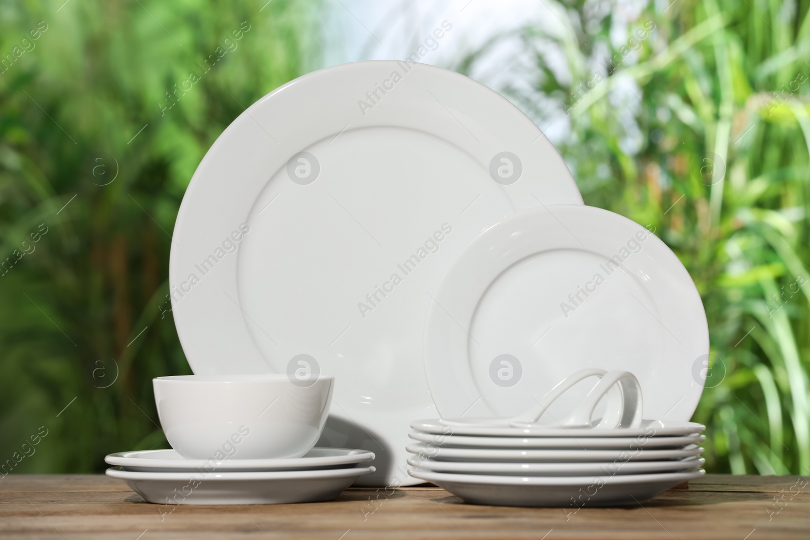 Photo of Set of clean dishware on wooden table against blurred background