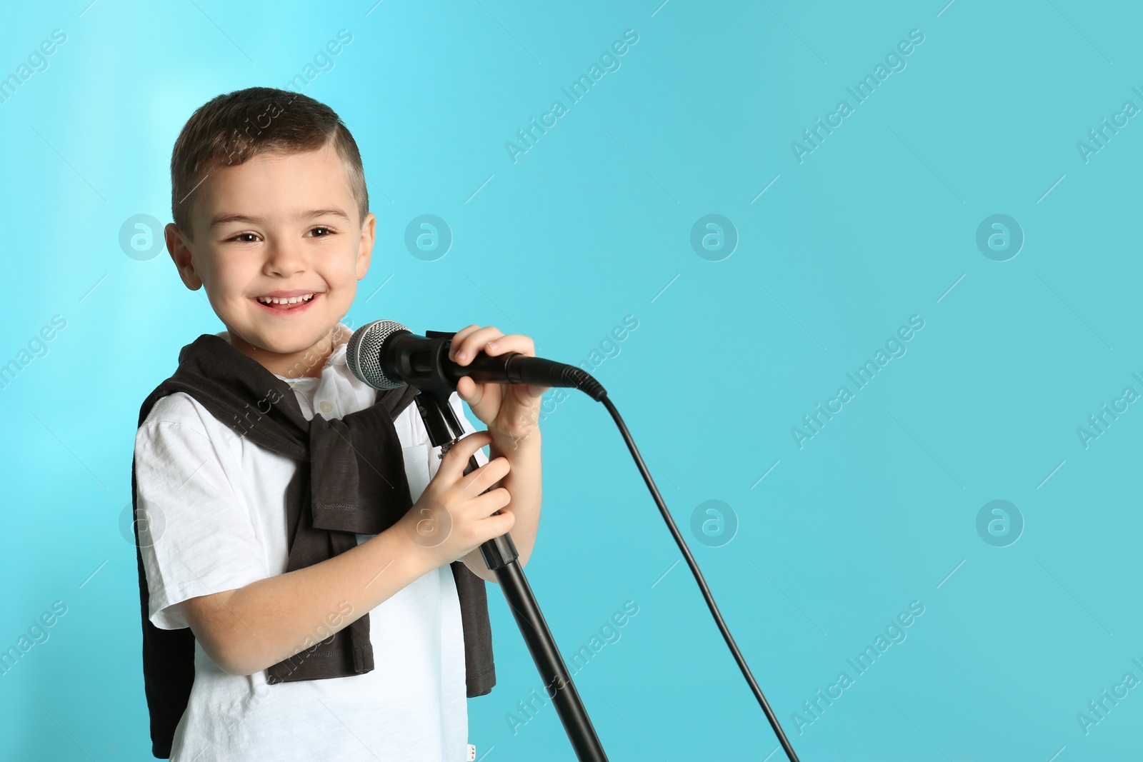 Photo of Cute funny boy with microphone on color background. Space for text